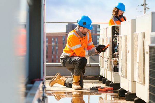 Technicians in safety gear inspecting rooftop HVAC units.